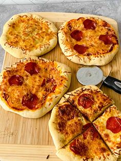 four small pizzas with pepperoni and cheese on a cutting board next to a knife