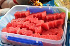 a plastic container filled with watermelon slices on top of a blue table cloth