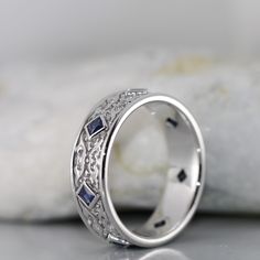 a white gold ring with blue sapphires and diamonds on the inside, sitting on a rock