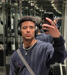 a young man wearing headphones taking a selfie in front of a mirrored wall