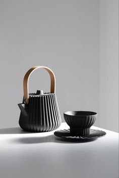 a tea pot and saucer sitting on a white countertop next to a black plate