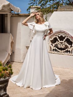 a woman in a white wedding dress standing on a patio with her hand on her head