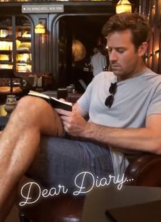 a man sitting in a chair with his legs crossed and reading a book that reads dear diary