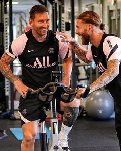 two men standing next to each other in a gym with exercise equipment on the floor