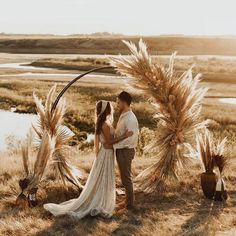 a bride and groom are standing in front of an arch made out of dried grass