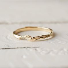 a gold wedding band with two leaves on it, sitting on top of a white surface