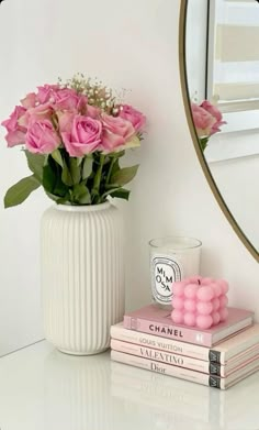 a white vase filled with pink roses next to two books