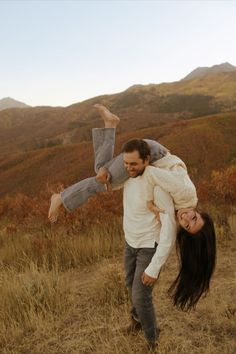 a man carrying a woman on his back in the middle of an open field with mountains in the background