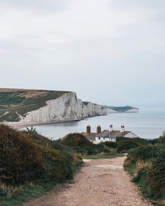 a dirt road leading to the beach with white cliffs in the background