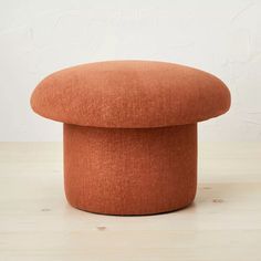 an orange round ottoman sitting on top of a wooden table next to a white wall