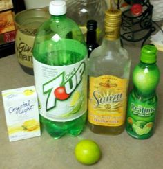 bottles of soda, lemonade and limes on a counter top next to an apple