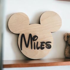 a wooden mickey mouse head with the word miles on it next to a teddy bear