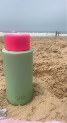 a green and pink cup sitting on top of a sandy beach