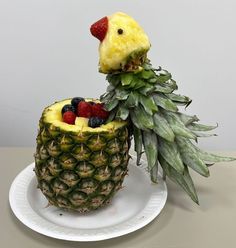 a pineapple shaped like a chicken sitting on top of a plate with fruit in it