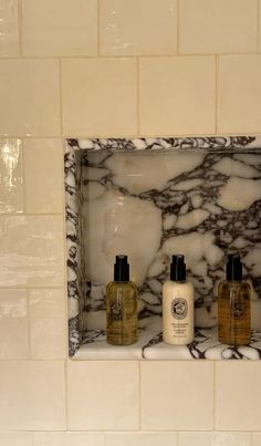 three bottles of hand soap and lotion on a shelf in a marble tiled bathroom