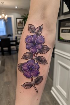 a woman's leg with purple flowers and leaves tattoo on the left side of her arm