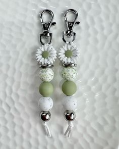 two white and green beads are attached to silver hooks on a white plate with flowers