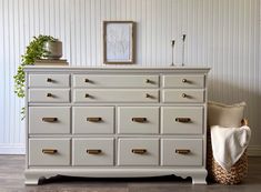 a white dresser with gold handles and knobs in a room next to a potted plant