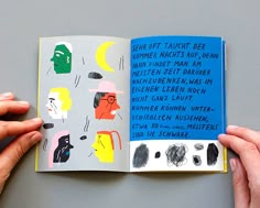 two hands are holding an open book with drawings on it and the pages have been colored blue