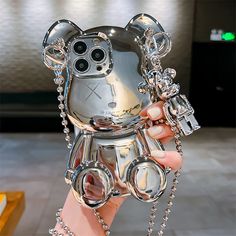 a person holding up a silver teddy bear phone case with chains on it's wrist