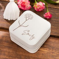 a small white box sitting on top of a wooden table next to flowers and a tassel