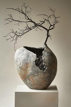 a vase with branches sticking out of it sitting on top of a white pedestal in front of a wall