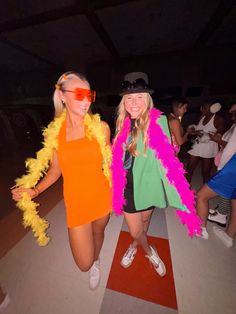 two women dressed in bright clothes and feather boas pose for the camera at a party