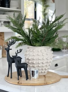 a white vase filled with green plants on top of a kitchen counter next to two black deer figurines