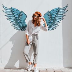 a woman standing next to a wall with wings painted on it