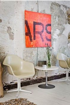 two chairs and a table in front of a wall with an art piece on it