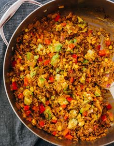 a skillet filled with rice and vegetables on top of a table next to a wooden spoon