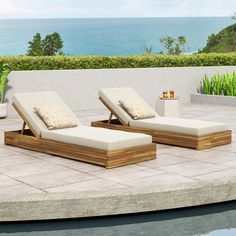 two chaise lounge chairs sitting on top of a stone patio next to the ocean