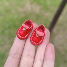 small red baby shoes sitting on top of someone's hand