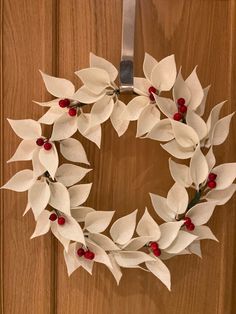 a white wreath with red berries hanging on a door