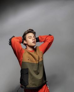 a young man is posing with his hands on his head while wearing an orange and black shirt