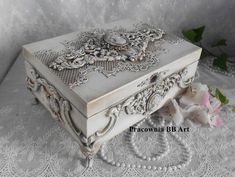 an ornate white box sitting on top of a lace covered tablecloth with flowers in the background