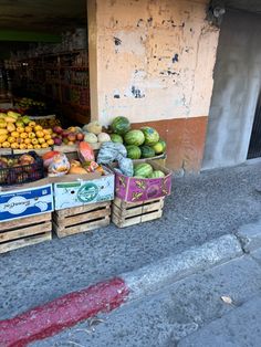 fruit and vegetables for sale on the side of the street in front of a building