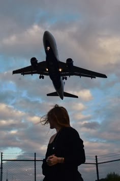 a woman is looking at her cell phone as an airplane flies overhead