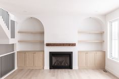 an empty living room with wooden shelves and a fireplace in the center, surrounded by wood flooring