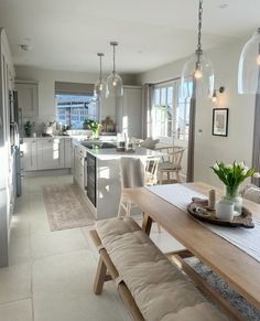 an open kitchen and dining room area with white cabinets, light wood table and bench