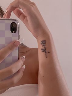 a woman with a small rose tattoo on her left arm holding a cell phone in front of her face