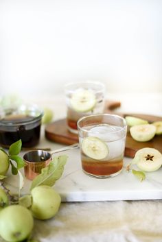 two glasses filled with apple cider on top of a marble tray next to apples