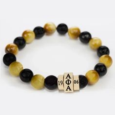 Beautiful Handmade Bracelet Features Various Shades Of Black And Gold Natural Stone Beads With A Bold Golden Centerpiece On A Sturdy Stretchable Elastic Band That Will Fit Most Wrists. The Centerpiece Is Made Of 3 Pieces That Features Alpha Phi Alpha In Greek Letters In The Center And 19 On One Side And 06 On The Other Side It Is A Subtle Piece That Is Perfect For Everyday Wear. Makes A Great Gift! Alpha Phi Alpha, Natural Stone Beads, Alpha Phi, Greek Letters, Bracelet Black, Mens Accessories Jewelry, Handmade Bracelet, Shades Of Black, Bead Bracelet