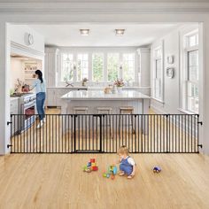 a woman standing in a kitchen next to a child playing with toys on the floor