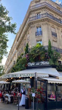 people sitting at tables in front of a building with plants growing on the side of it