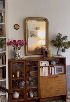 a room with a mirror, bookshelf and vases filled with flowers on top of it