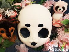 two stuffed animals and a white mask on a table with pink flowers, leaves and other stuff animals