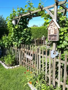 a bird house is hanging on a wooden trellis in the grass near a fence