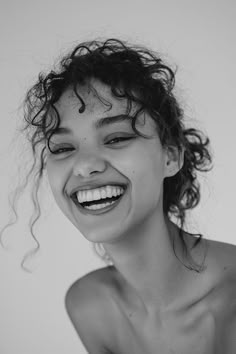 a smiling woman with curly hair and no shirt is looking at the camera while she has her eyes closed