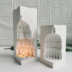 two small candles are sitting next to each other in front of a white building with a dome on top